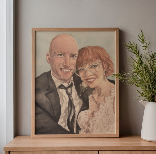 watercolor painting with a man and woman smiling on their wedding day. it is framed on a table or desk