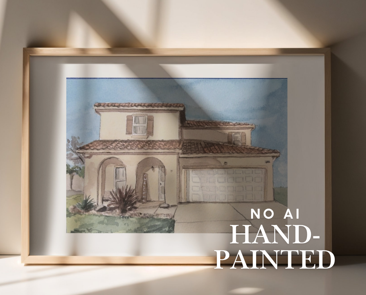 A framed hand-painted watercolor illustration of a Mediterranean-style house, displayed on a shelf against a beige wall with dramatic window shadows. The print features a light wood frame and a white mat, with the text 'NO AI HAND-PAINTED' overlaid on the bottom right.